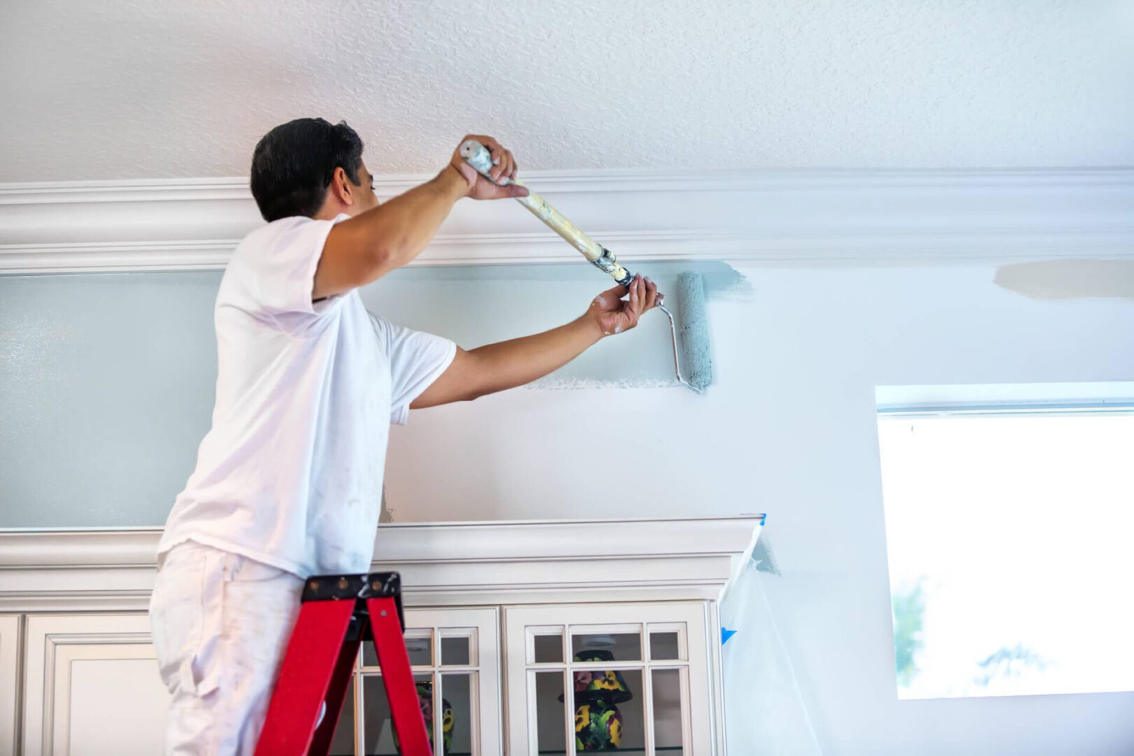 Painter on ladder painting wall near molding