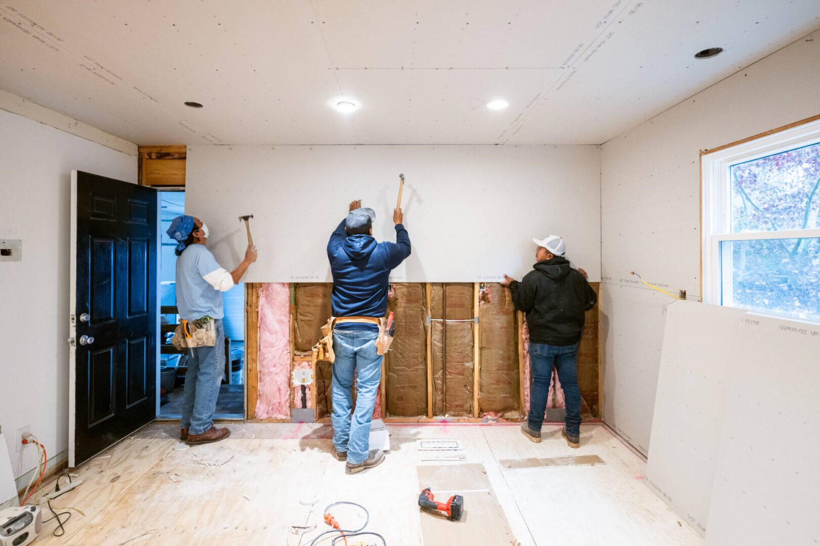 Three workers installing drywall over insulated wall
