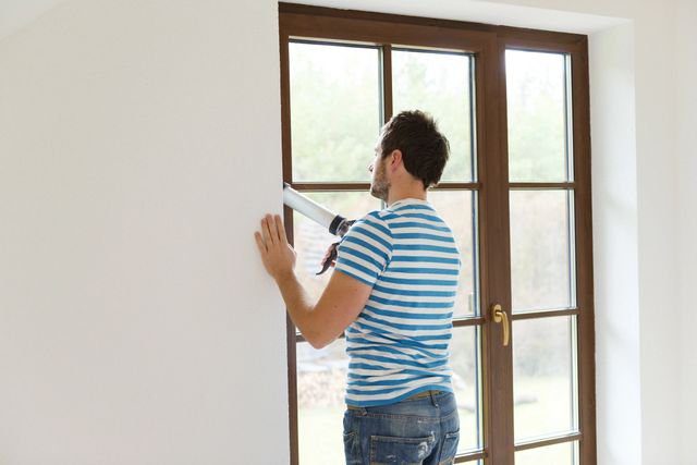 Man sealing interior window with caulk gun