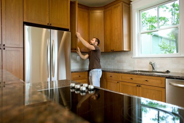Man reaching into upper wooden kitchen cabinet