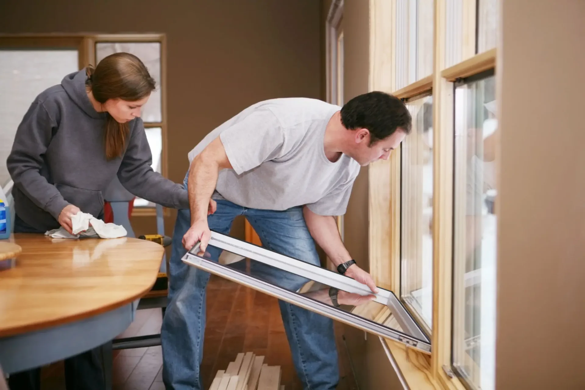 Man replacing window sash while woman cleans
