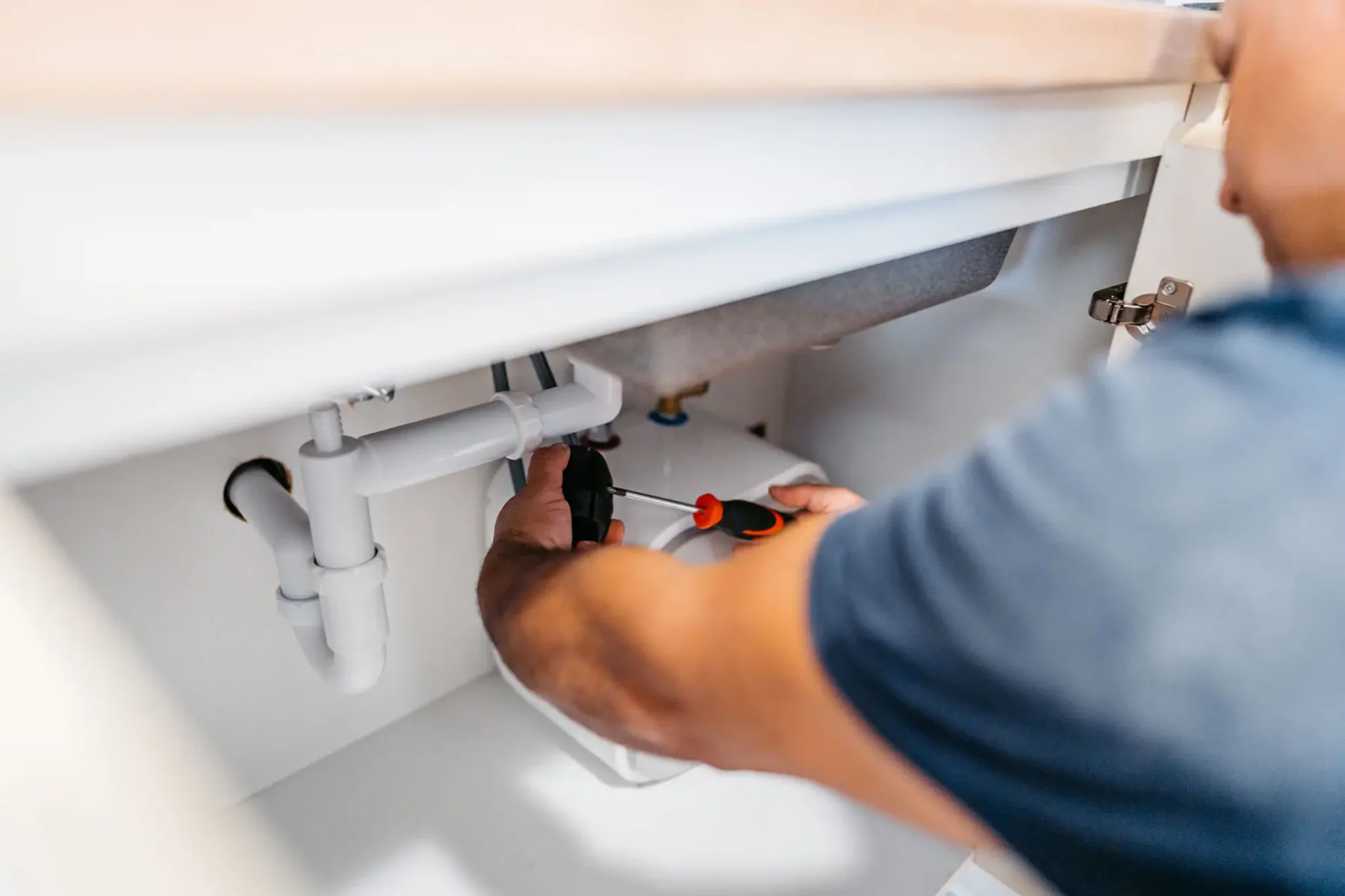 Plumber repairing under-sink plumbing with screwdriver