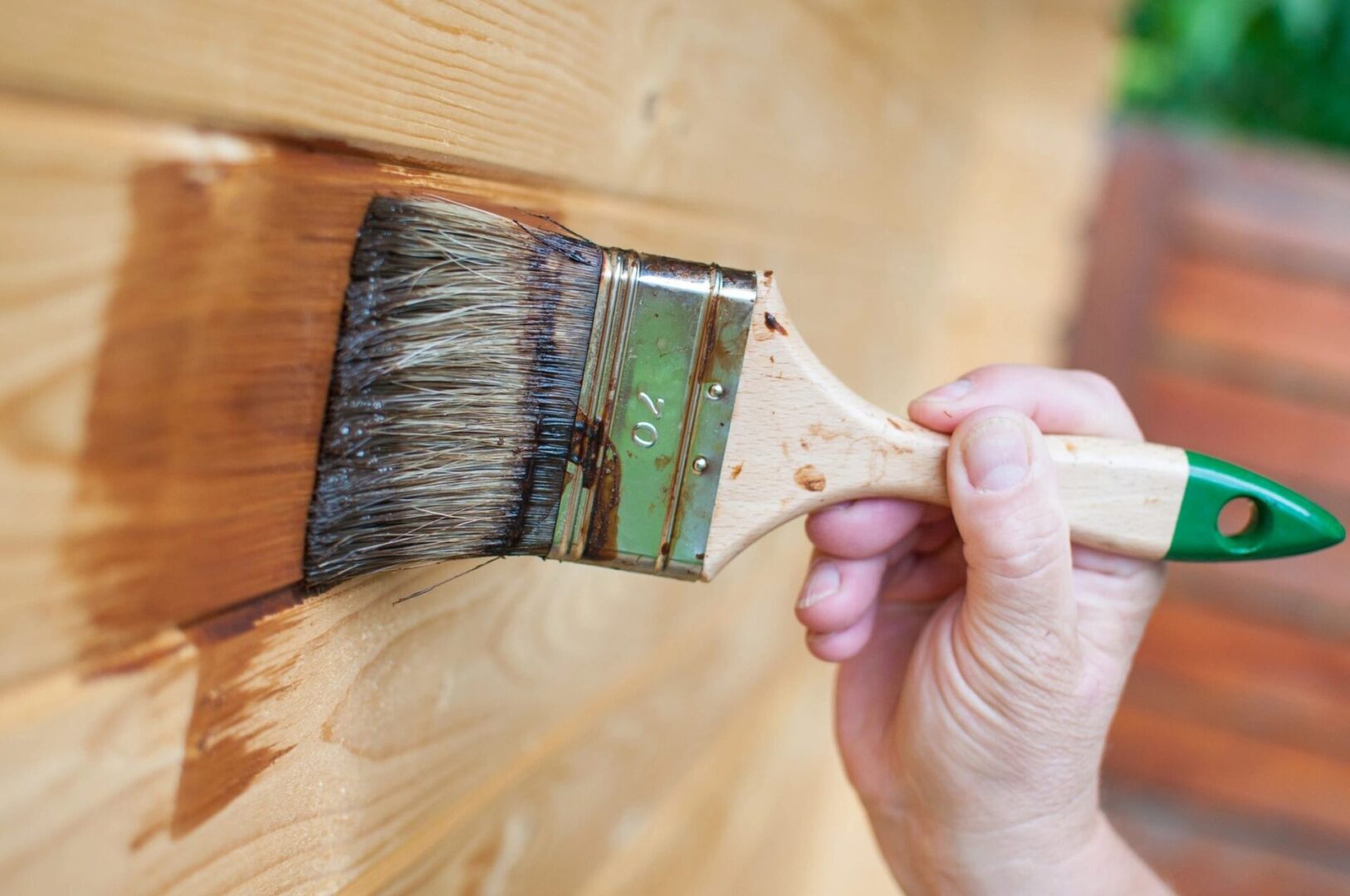 Hand brushing wood stain onto fence panels